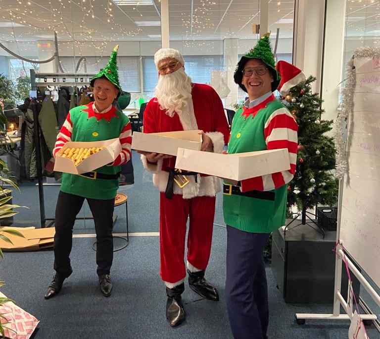 Foto van Aad de Groot, Jako Papac en Joop le Conge die in kerstverkleding lekkernijen uitdelen. 